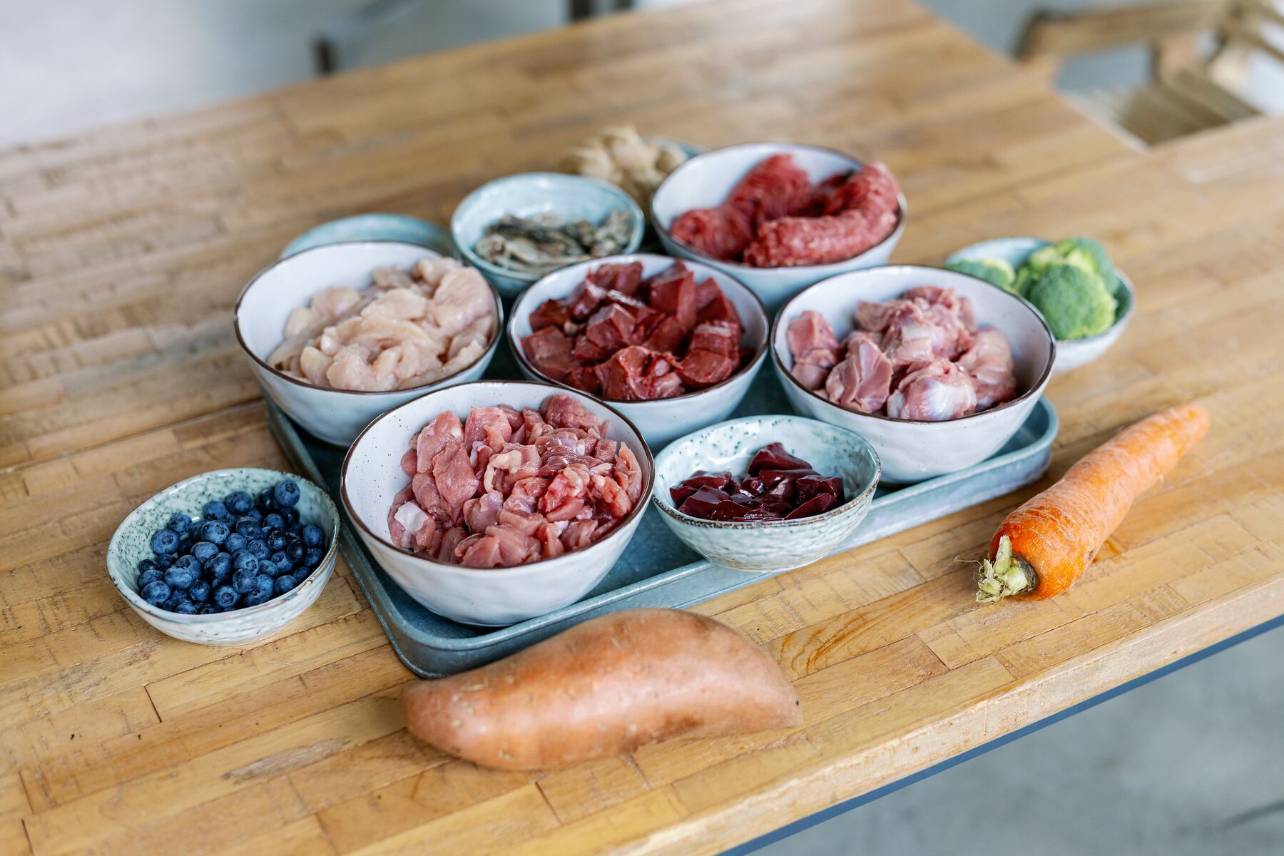 Bowls of fresh meat, organs, vegetables and berries laid out on a wooden kitchen table