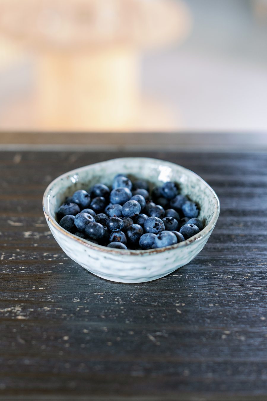 A small ceramic bowl of fresh blueberries on a dark wooden table