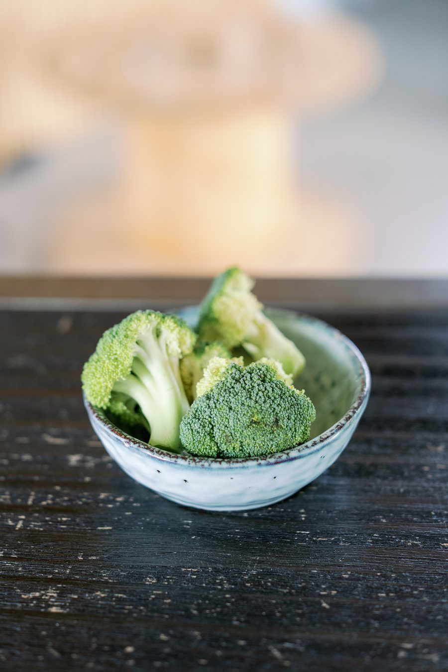 A small ceramic bowl of fresh broccoli florets on a dark wooden table