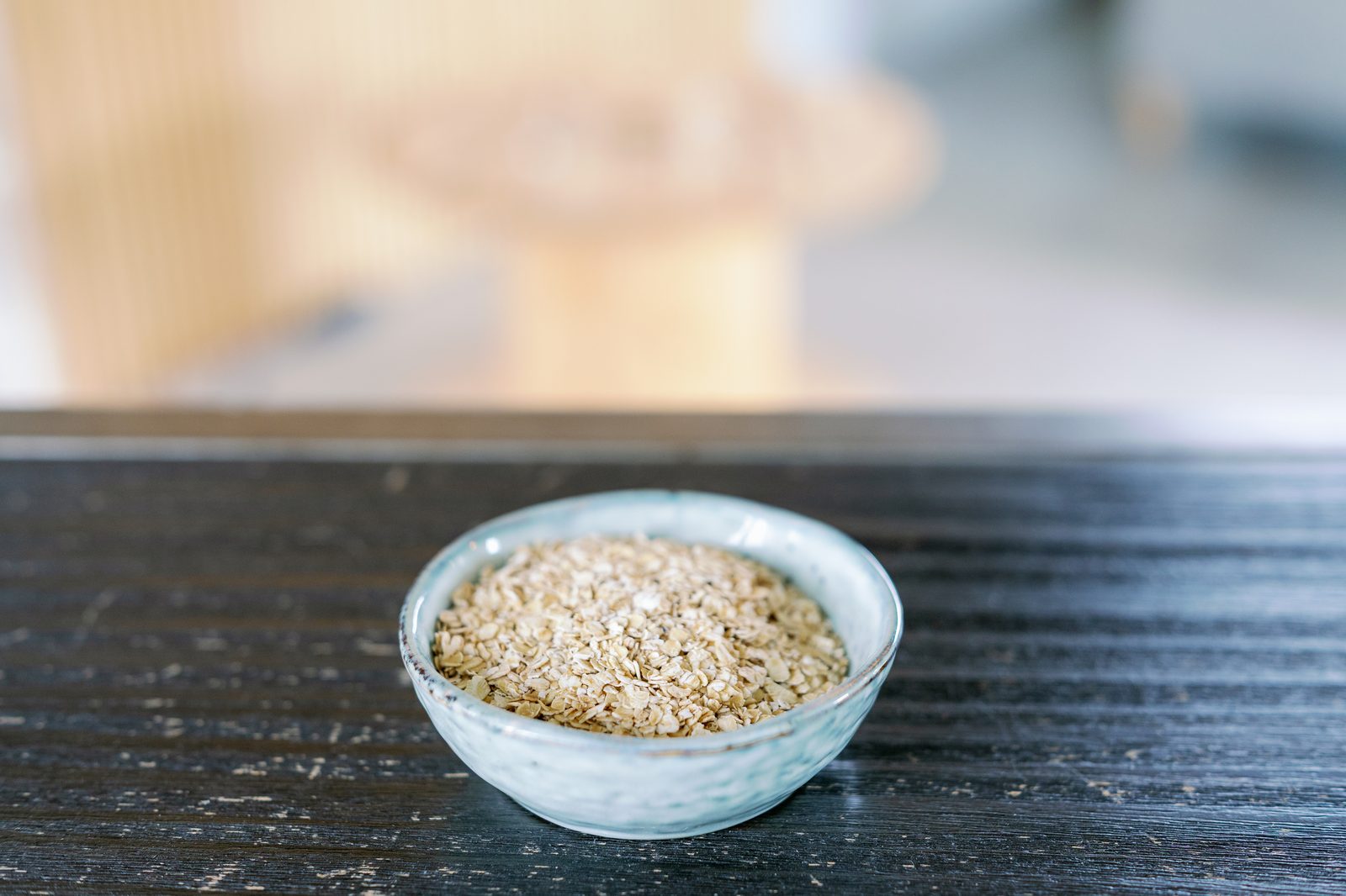 A small ceramic bowl of rolled oats on a dark wooden table