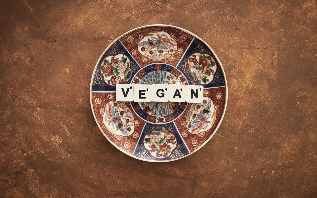 A decorated porcelain plate with letter tiles on it spelling the word VEGAN